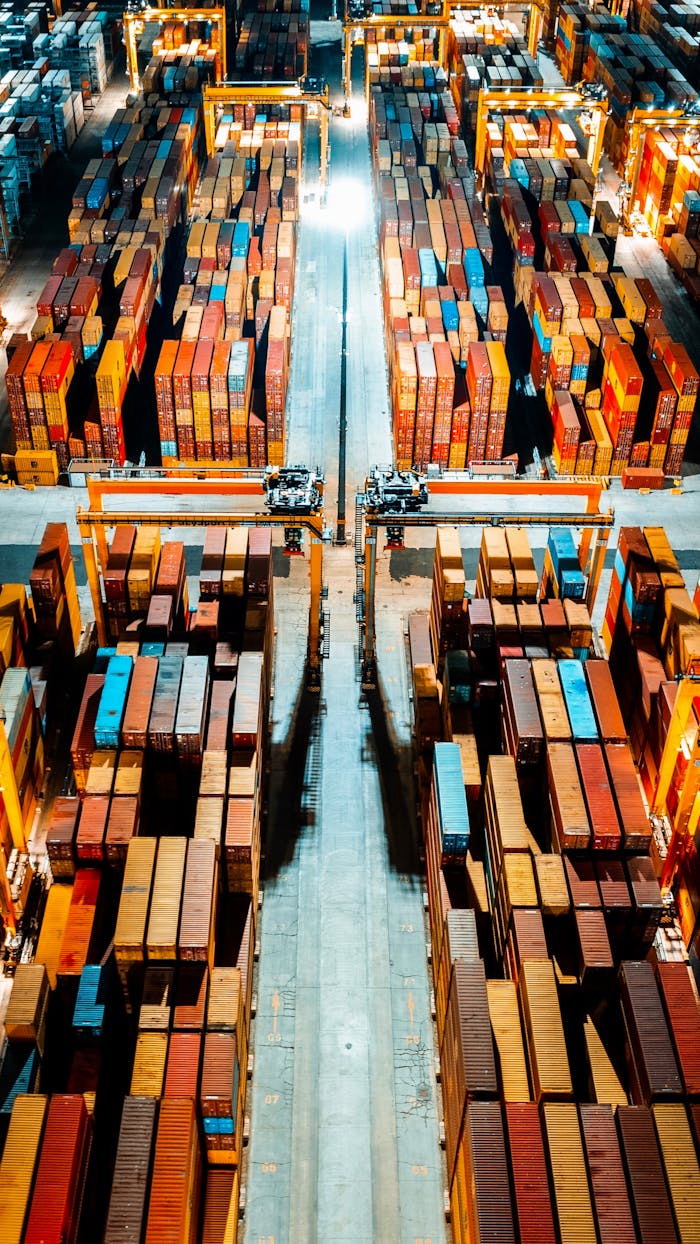 Aerial view of organized cargo containers in a brightly lit warehouse at night.